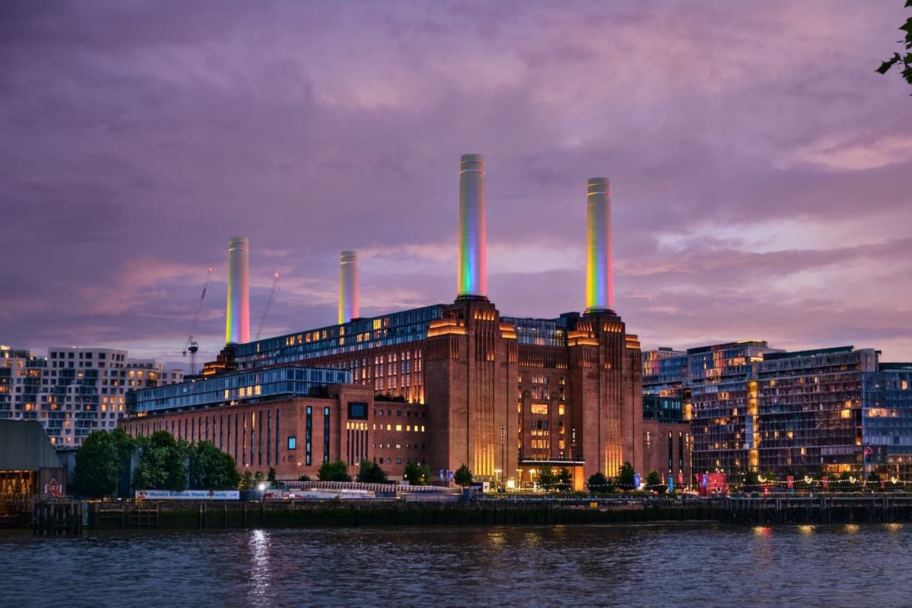 Battersea Power Station at blue hour, its four chimneys lit and reflected in the Thames